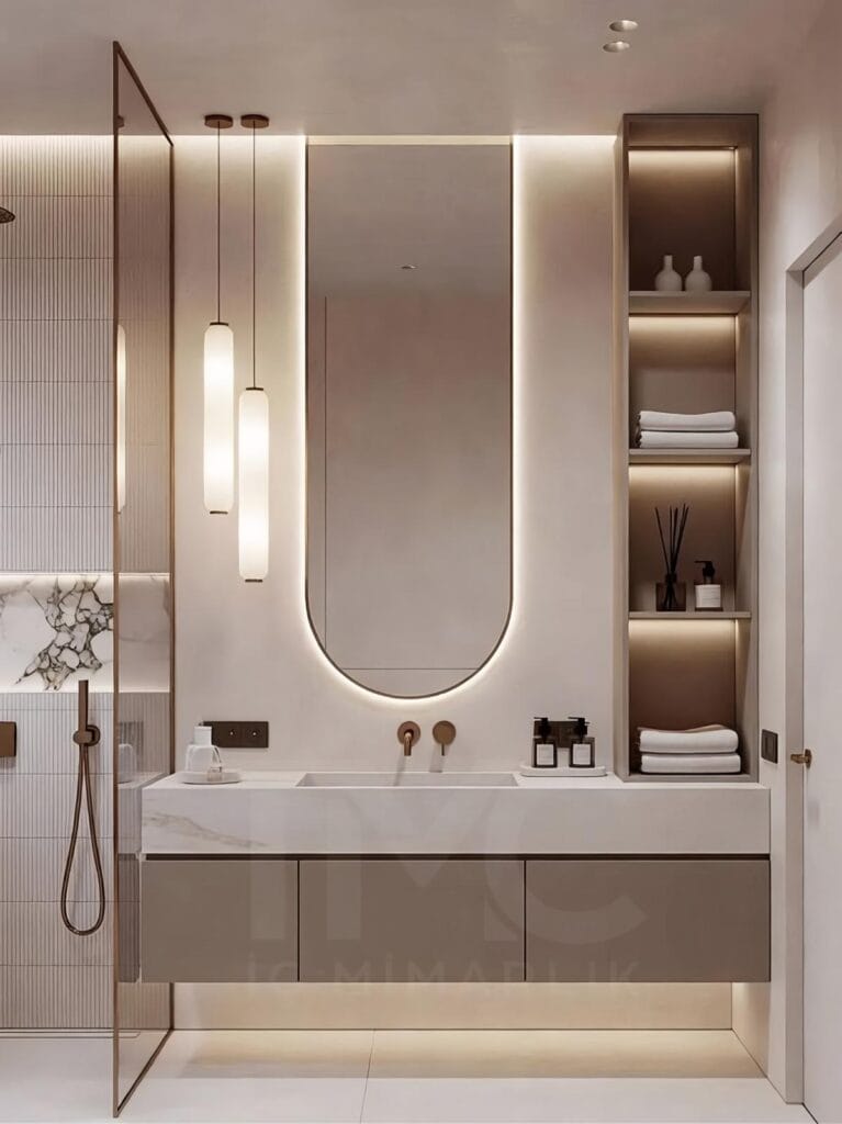 Toskana Vadisi Evleri’nde Selin & Emre için tasarlanan modern banyo; vizon tonlu dolap, mermer tezgah, arkadan LED aydınlatmalı oval ayna ve nervür panel detaylarıyla lüks ve sade iç mimari tasarım.
