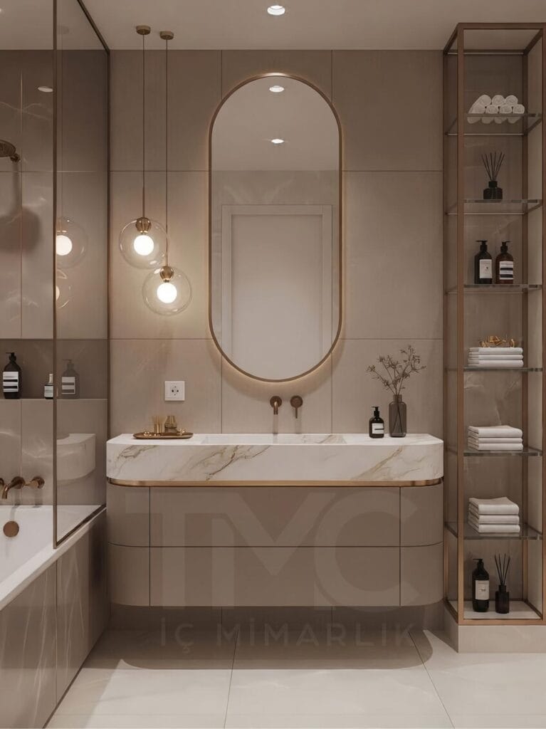 Toskana Vadisi Evleri’nde Selin & Emre için tasarlanan modern banyo; vizon tonlu dolap, mermer tezgah, arkadan LED aydınlatmalı oval ayna ve nervür panel detaylarıyla lüks ve sade iç mimari tasarım.