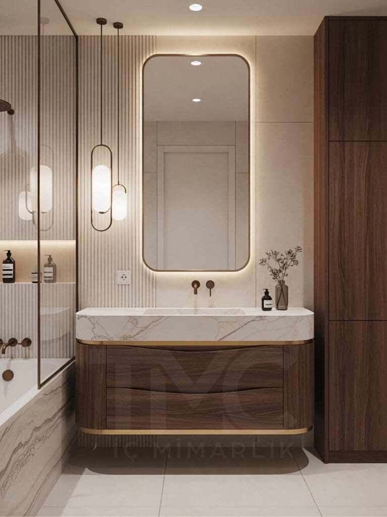 Toskana Vadisi Evleri’nde Selin & Emre için tasarlanan modern banyo; vizon tonlu dolap, mermer tezgah, arkadan LED aydınlatmalı oval ayna ve nervür panel detaylarıyla lüks ve sade iç mimari tasarım.