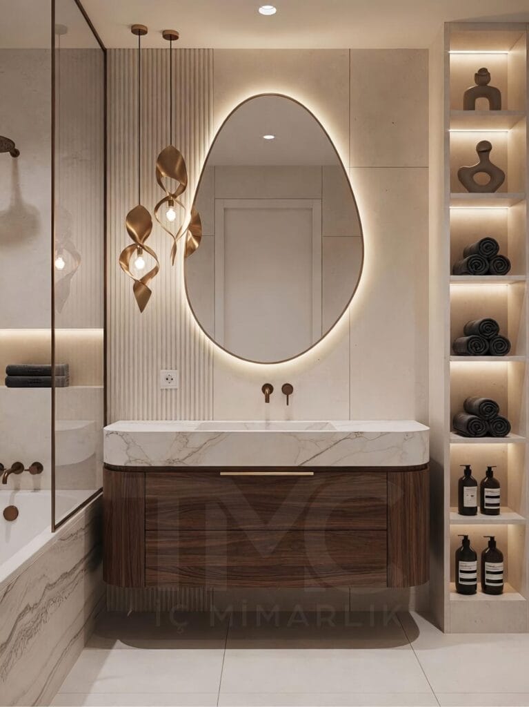 Toskana Vadisi Evleri’nde Selin & Emre için tasarlanan modern banyo; vizon tonlu dolap, mermer tezgah, arkadan LED aydınlatmalı oval ayna ve nervür panel detaylarıyla lüks ve sade iç mimari tasarım.
