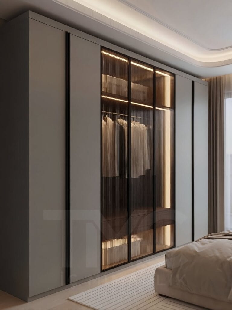 Modern lüks yatak odası tasarımı, Park Residences Cadde projesinde Tunç & Arzu çifti için özel üretim olarak tasarlanan sıcak ceviz detaylı, nervür cam giyinme dolaplı, LED aydınlatmalı modern yatak odası iç mimari projesi. Soft krem tonları, bronz detaylar, doğal mermer yüzeyler ve ölçüye özel depolama çözümleriyle premium yaşam alanı tasarımı. TMC Mimarlık özel tasarım yatak odası uygulaması.